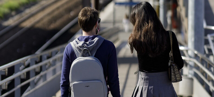 Photo de deux voyageurs avec leurs bagages, vus de dos, en gare.